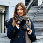 Stijlvolle zwarte leren auto handschoenen voor dames, gedragen in een elegante look met blauwe jas en sjaal.