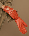 Women's orange lambskin glove close-up with touchscreen panel on thumb