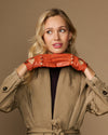 Women's orange lambskin driving gloves laid across wrists, snap-button cuffs