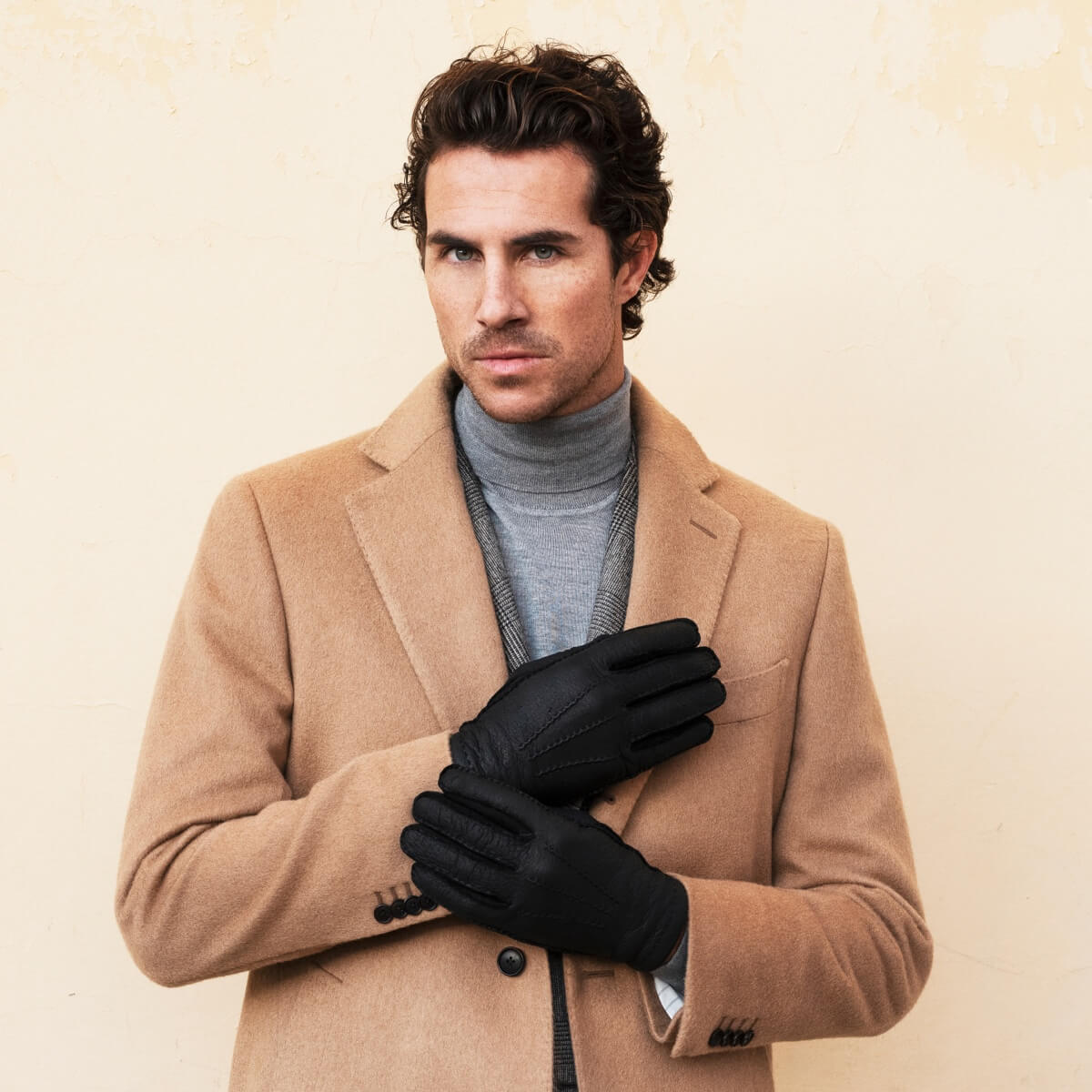 Men’s dark leather gloves worn with a tan coat and gray turtleneck