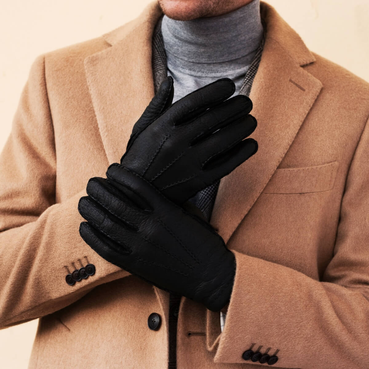 Men’s dark leather gloves on hands, shown with tan coat sleeves
