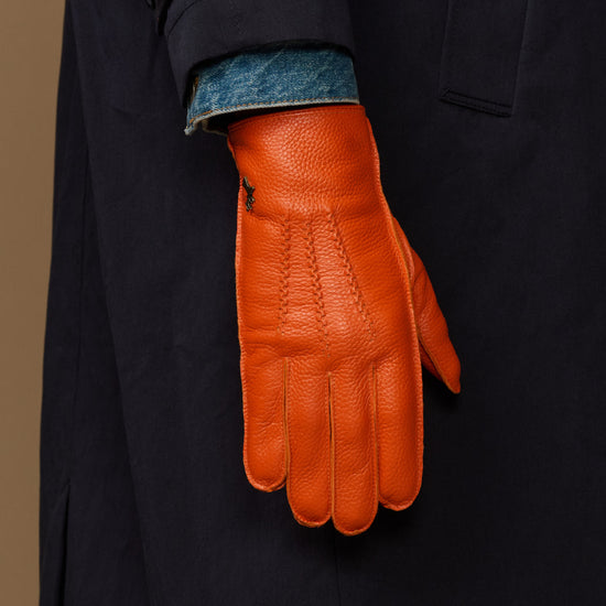 Orange leather gloves with blue cuff lining on dark sleeve, side view