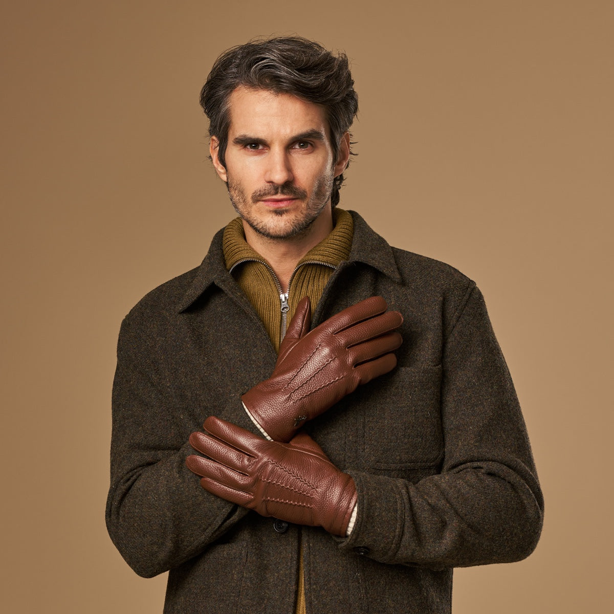 Brown deerskin leather gloves with cream knit lining peeking at wrist