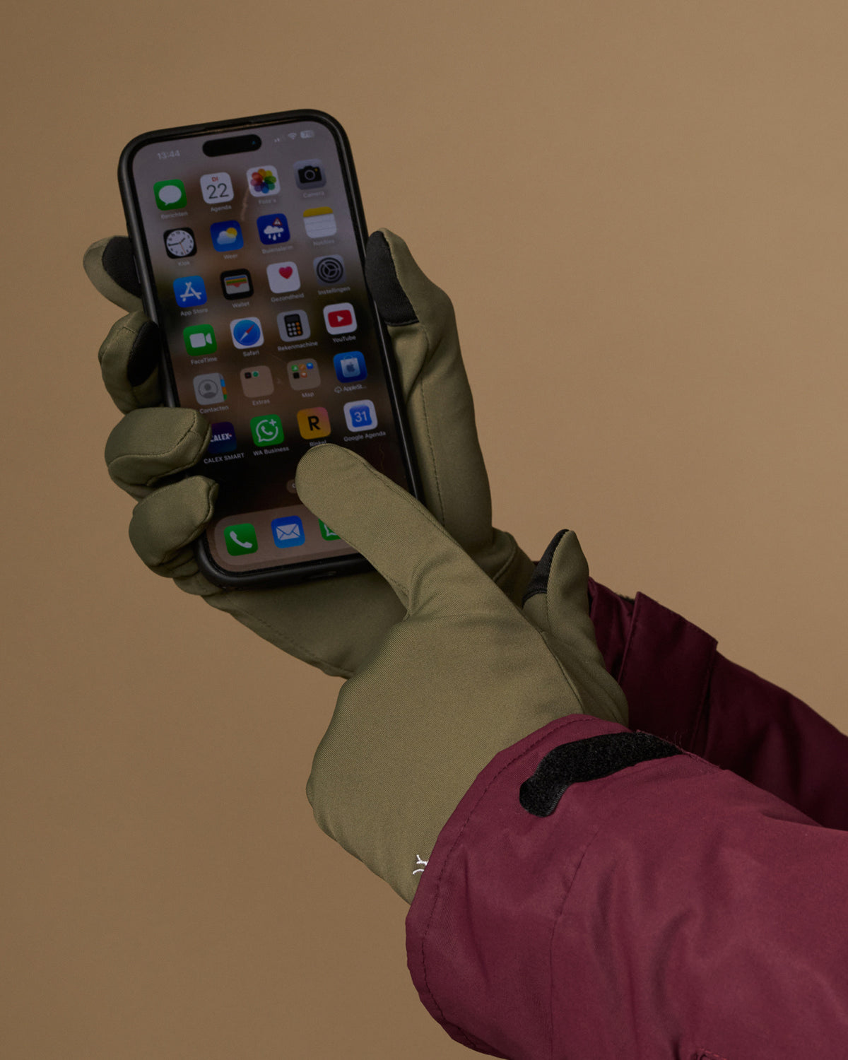 Olive green activity gloves operate a smartphone with touchscreen fingertips