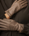 Taupe leather gloves close-up showing gold-tone buckle cuffs and seam detailing