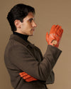 Men's orange lambskin driving gloves with touchscreen, worn palm-out
