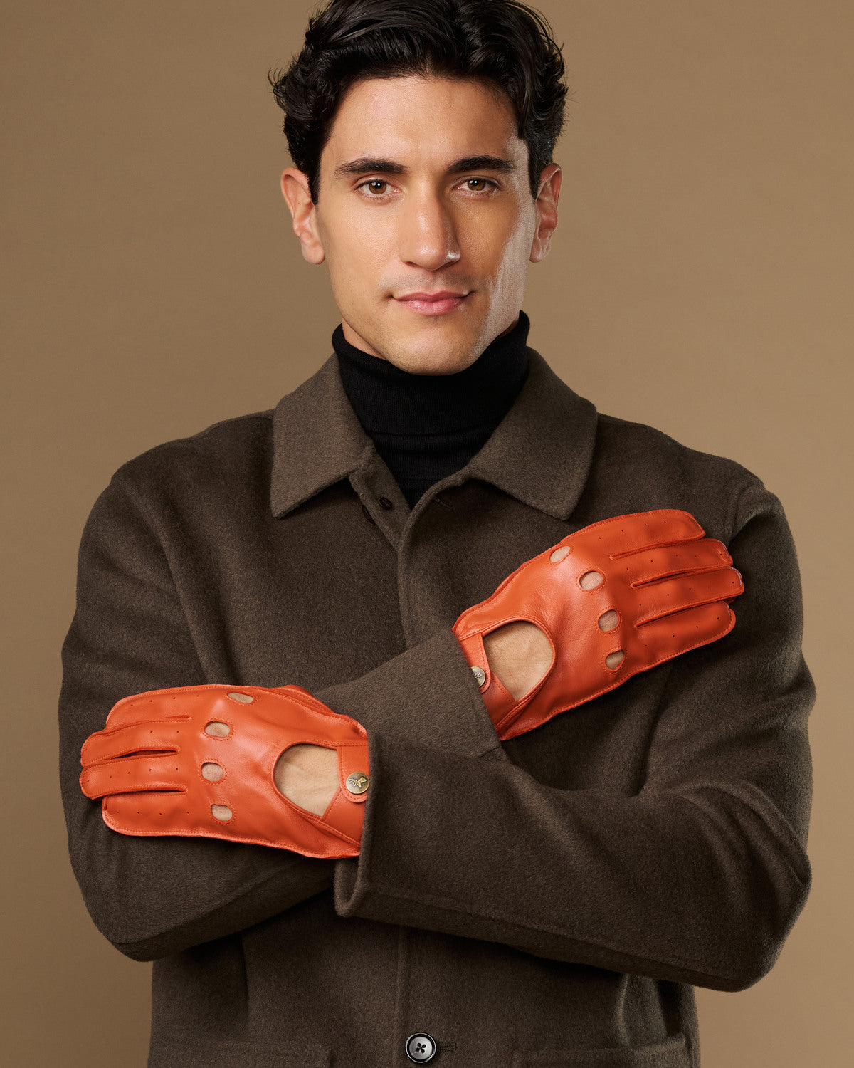 Men's orange lambskin driving gloves with touchscreen, worn with crossed arms