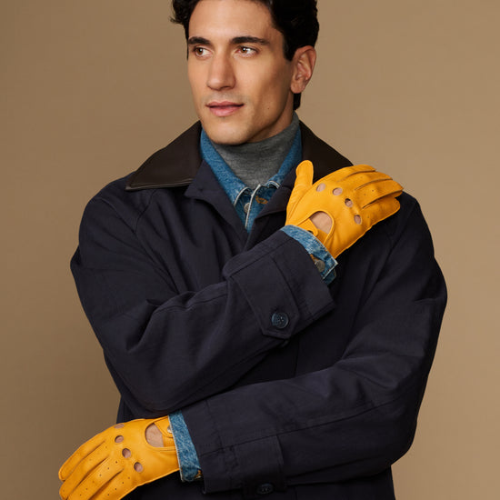 Men's yellow lambskin driving gloves worn with a navy coat, perforated knuckles