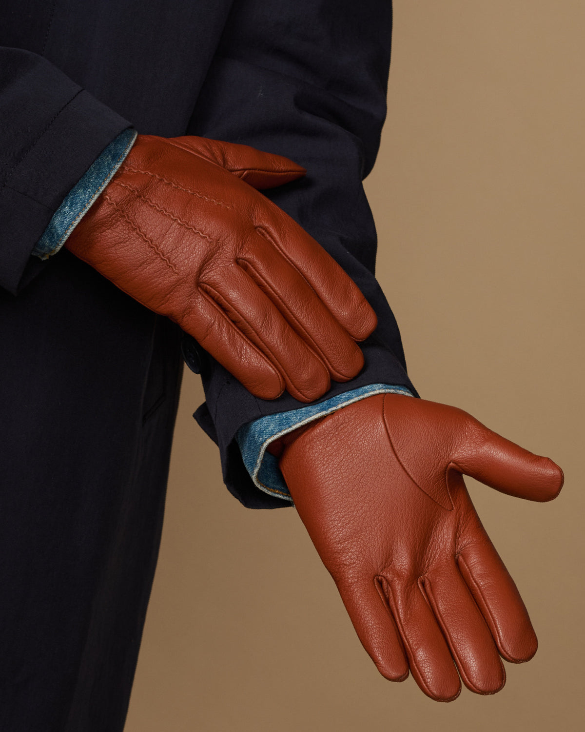 Cognac leather glove close-up with stitched fingers, wool cuff trim, touchscreen