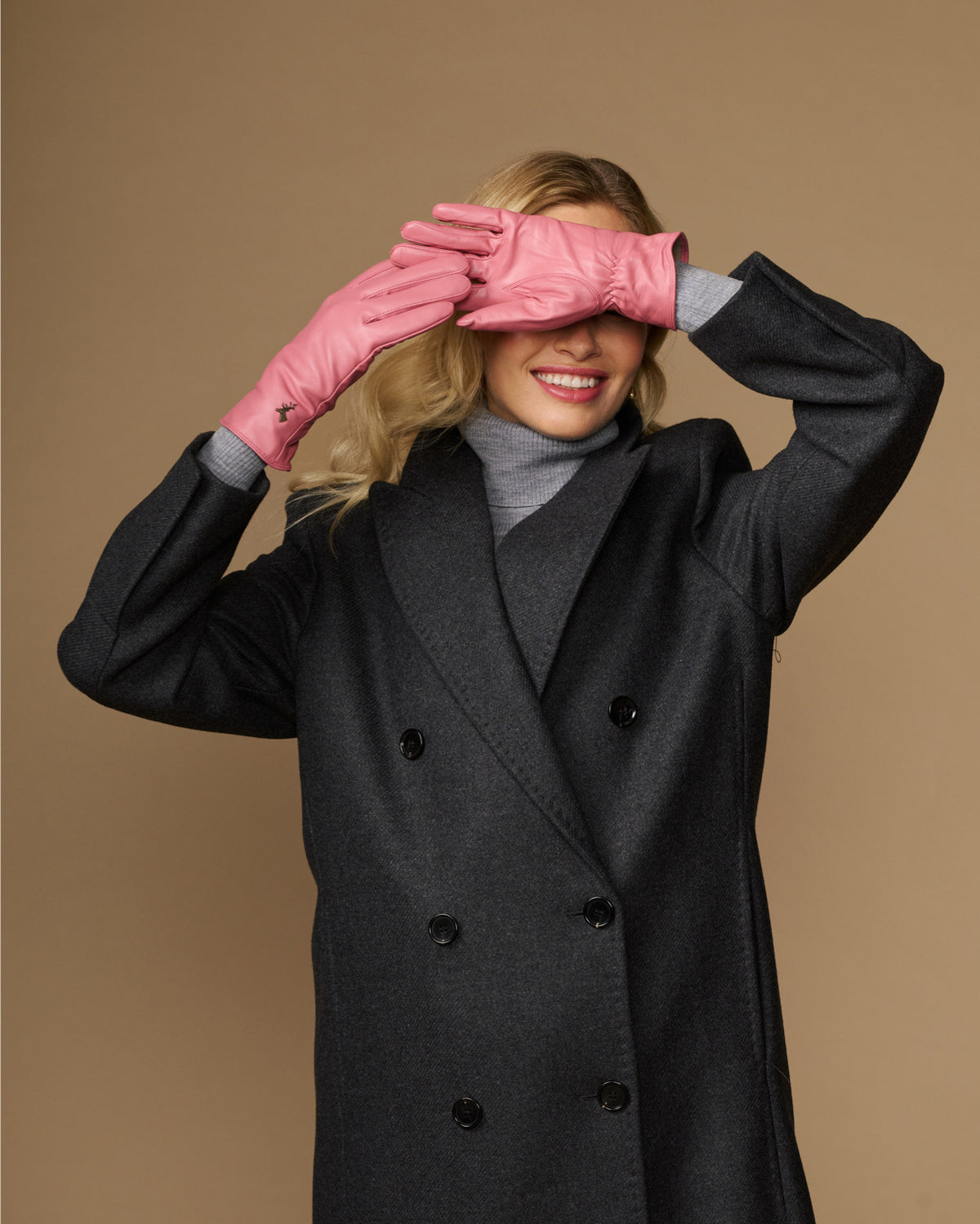 Women’s pink leather gloves covering eyes, with small logo on back of hand