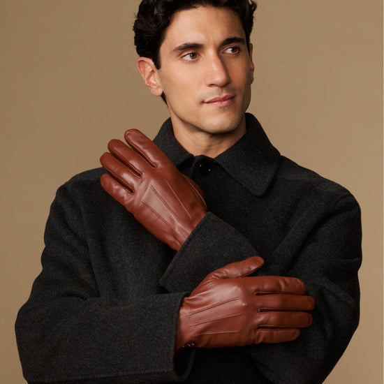 Cognac leather gloves with fleece-lined cuffs, worn by model with both hands raised