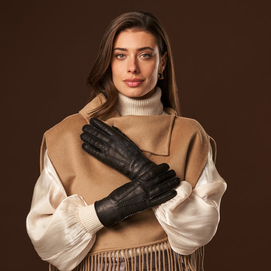 Woman wearing black leather gloves with short cuffs and gold wrist emblem