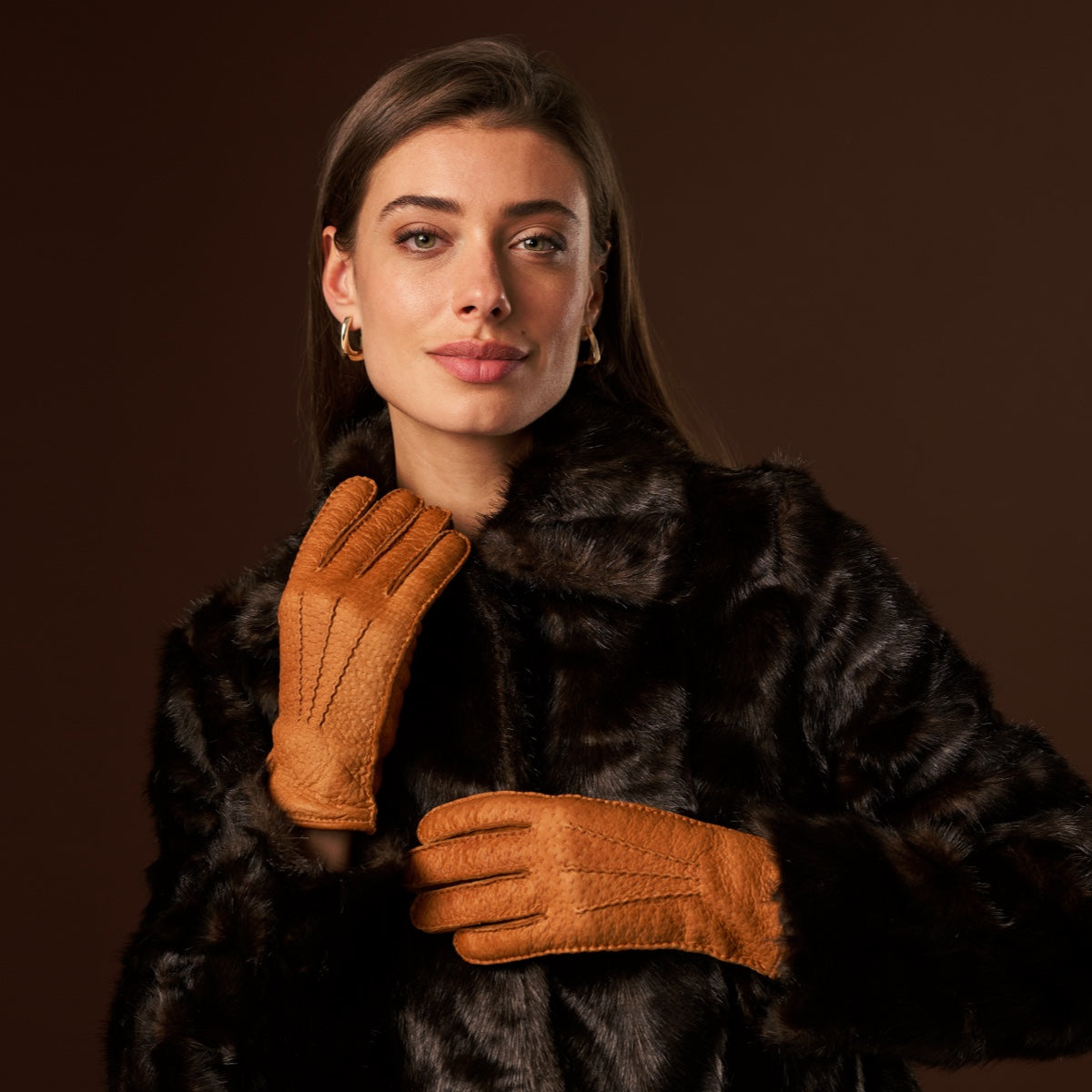 Cognac leather gloves held near the chest, short cuff with stitched fingers