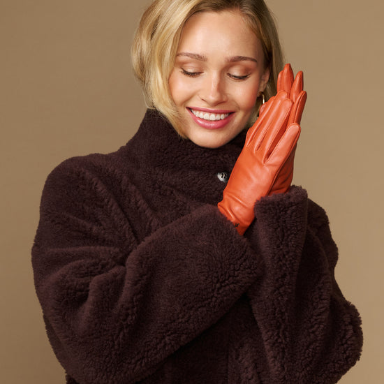 Lauren orange lambskin leather gloves with touchscreen tips, silk-lined, posed on hands