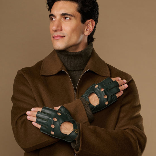 Dark green lambskin driving gloves with open fingertips and perforations, worn crossed over the chest