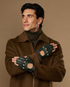 Dark green lambskin driving gloves with open fingertips and perforations, worn crossed over the chest