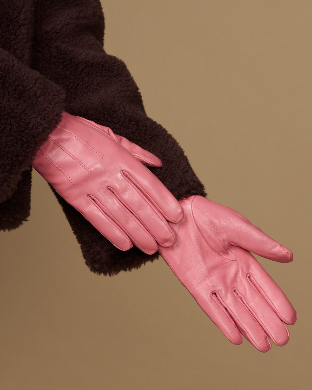 Pink leather glove close-up with stitched fingers and dark cuffs
