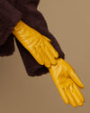 Close-up of yellow leather gloves with stitched fingers and dark plush cuff lining