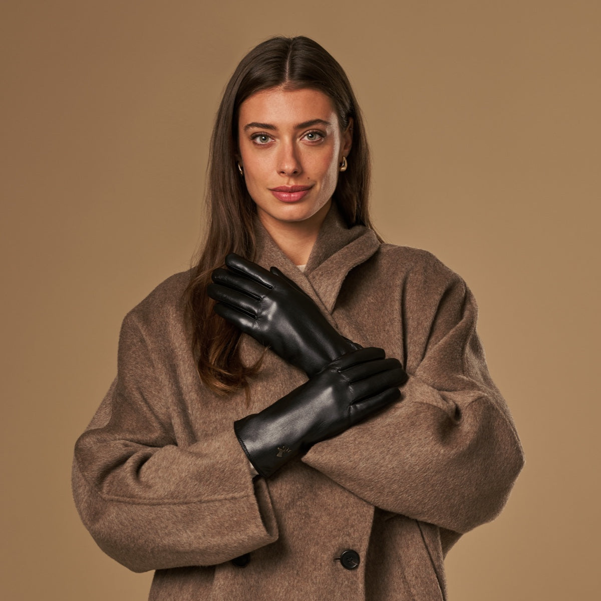 Black vegan leather gloves on hands against a tan coat backdrop