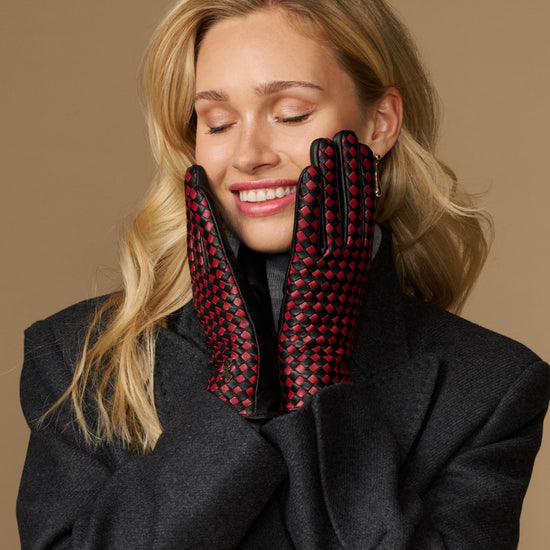 Women's black leather gloves with red-and-black checkered lining held near the face