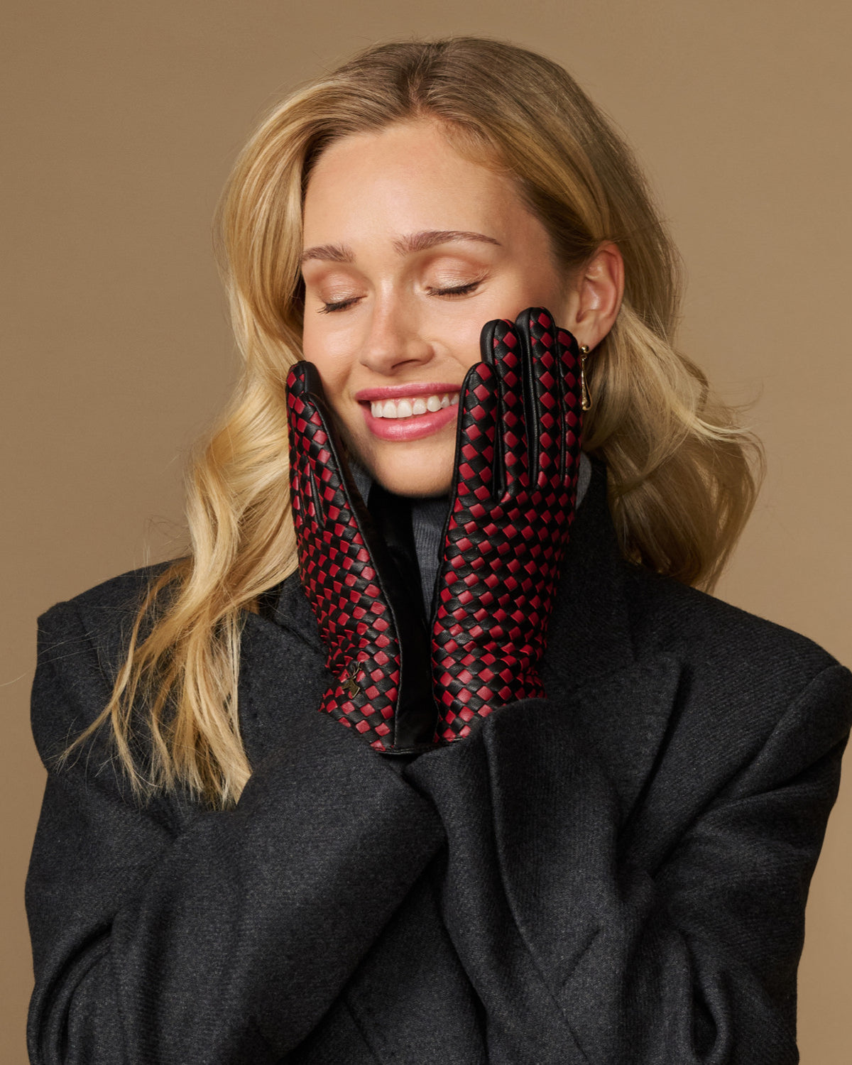 Women's black leather gloves with red-and-black checkered lining held near the face