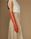 Orange leather elbow-length glove on arm with smooth surface and tapered fingers