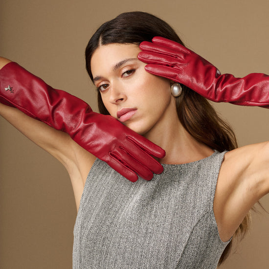 Pair of red leather gloves raised near face, showing knuckle shaping and slim fit