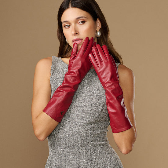 Red below-elbow leather gloves held together near face, showing glossy leather texture