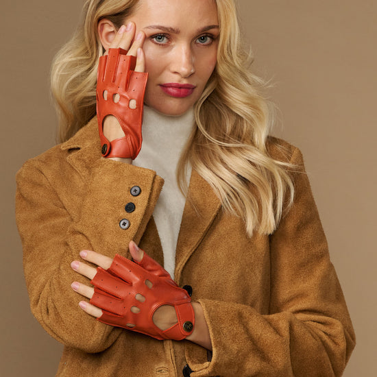 Orange fingerless driving gloves on model, thumb and finger cutouts with wrist strap