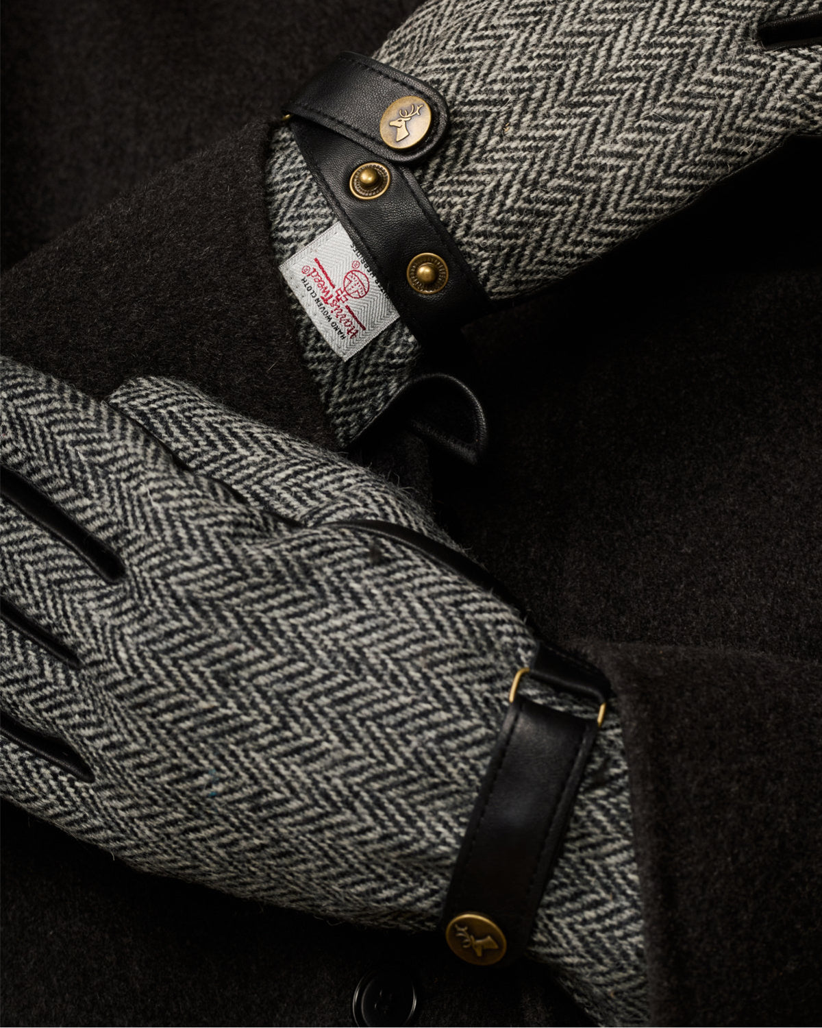 Men's gloves close-up: black leather cuff with gold snaps and gray herringbone panel.