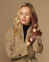 Brown leather driving gloves on model with elastic wrist and brass button cuff detail