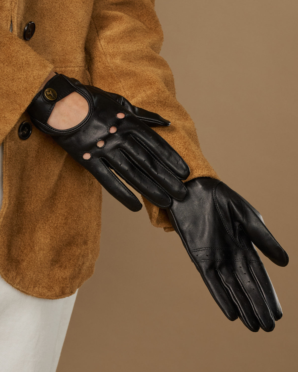Black leather driving gloves with oval buckle emblem and button-studded cuff opening.
