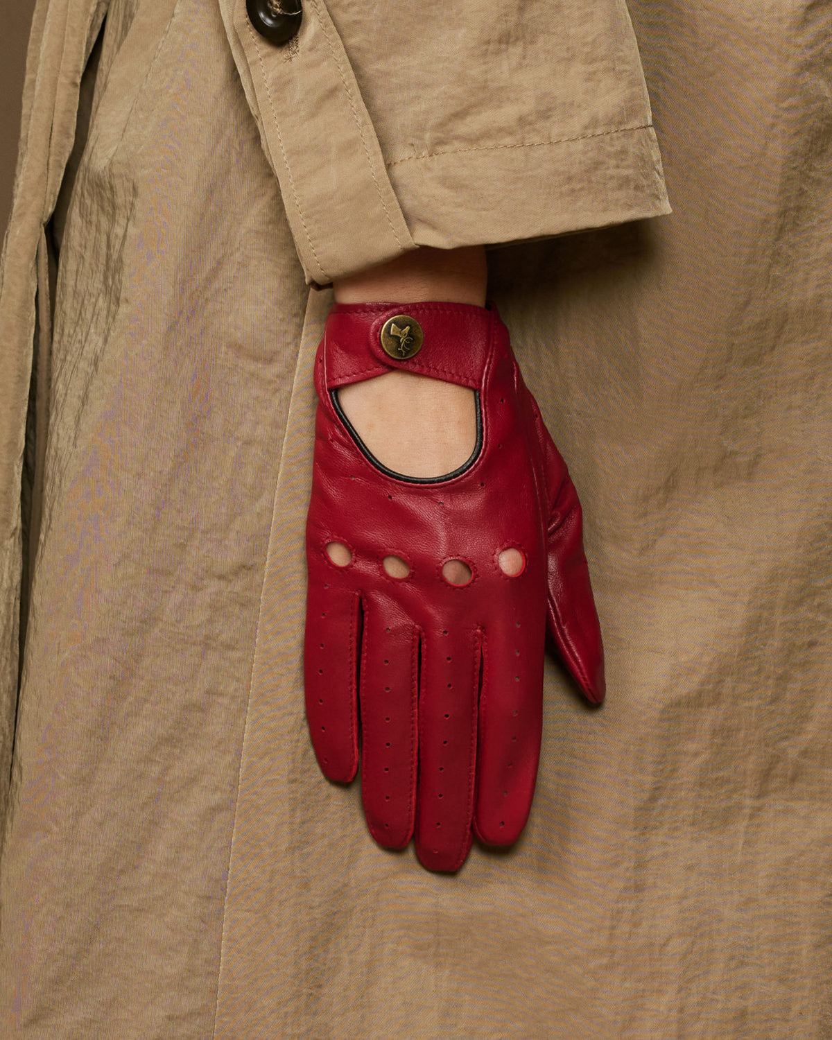Red leather driving glove with open knuckle panel and round button emblem on cuff
